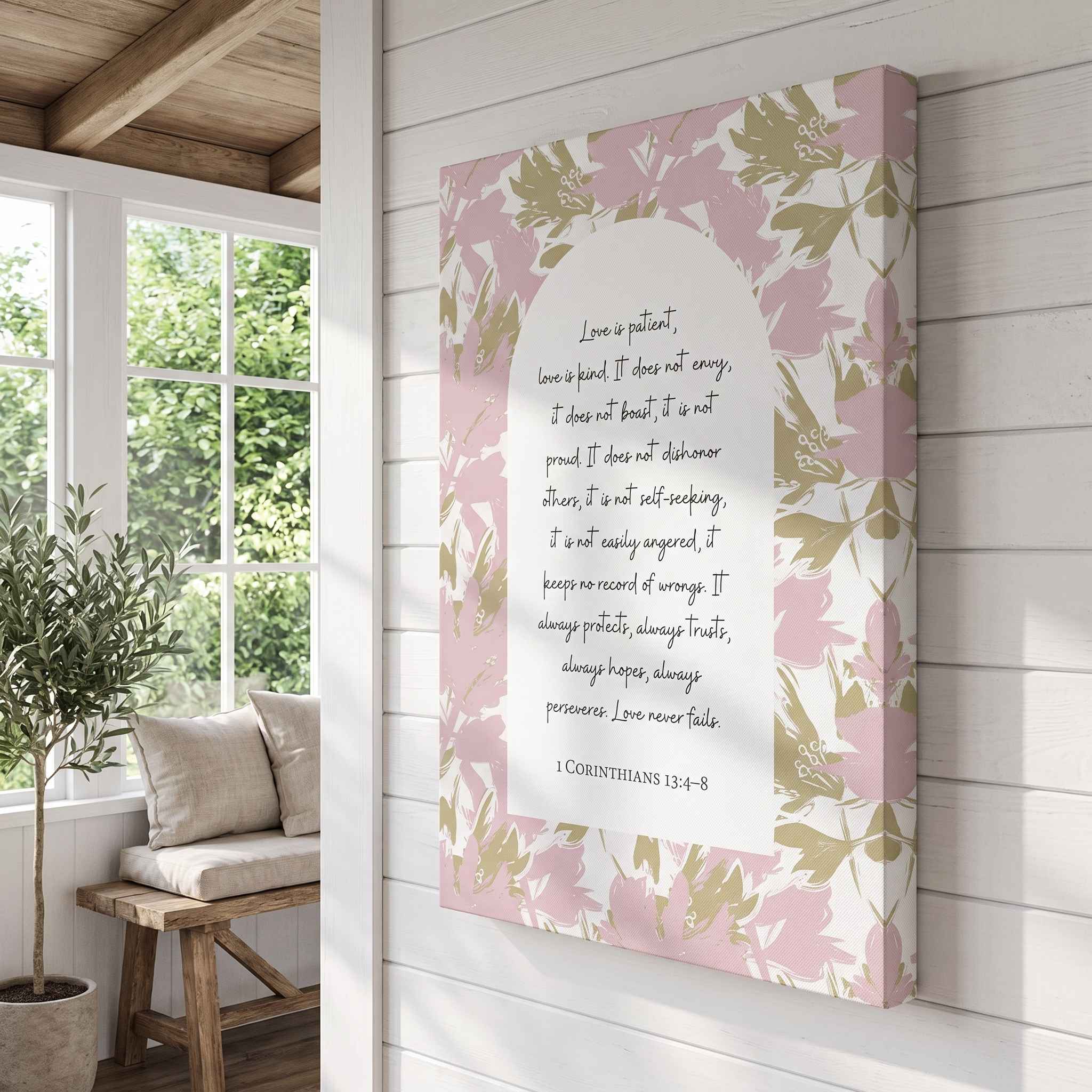 Christian floral unframed canvas wall art titled 1 Corinthians 13:4–8 featuring "Love is patient, love is kind" with pink and sage botanical artwork, displayed on a white wood-paneled wall in a bright Scandinavian sunroom.