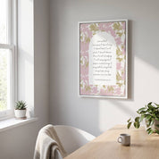 Framed Christian floral wall art titled 1 Corinthians 13:4–8 featuring "Love is patient, love is kind" with pink and sage botanical artwork, displayed in a white frame on a light gray wall above a wooden desk in a bright Scandinavian office.