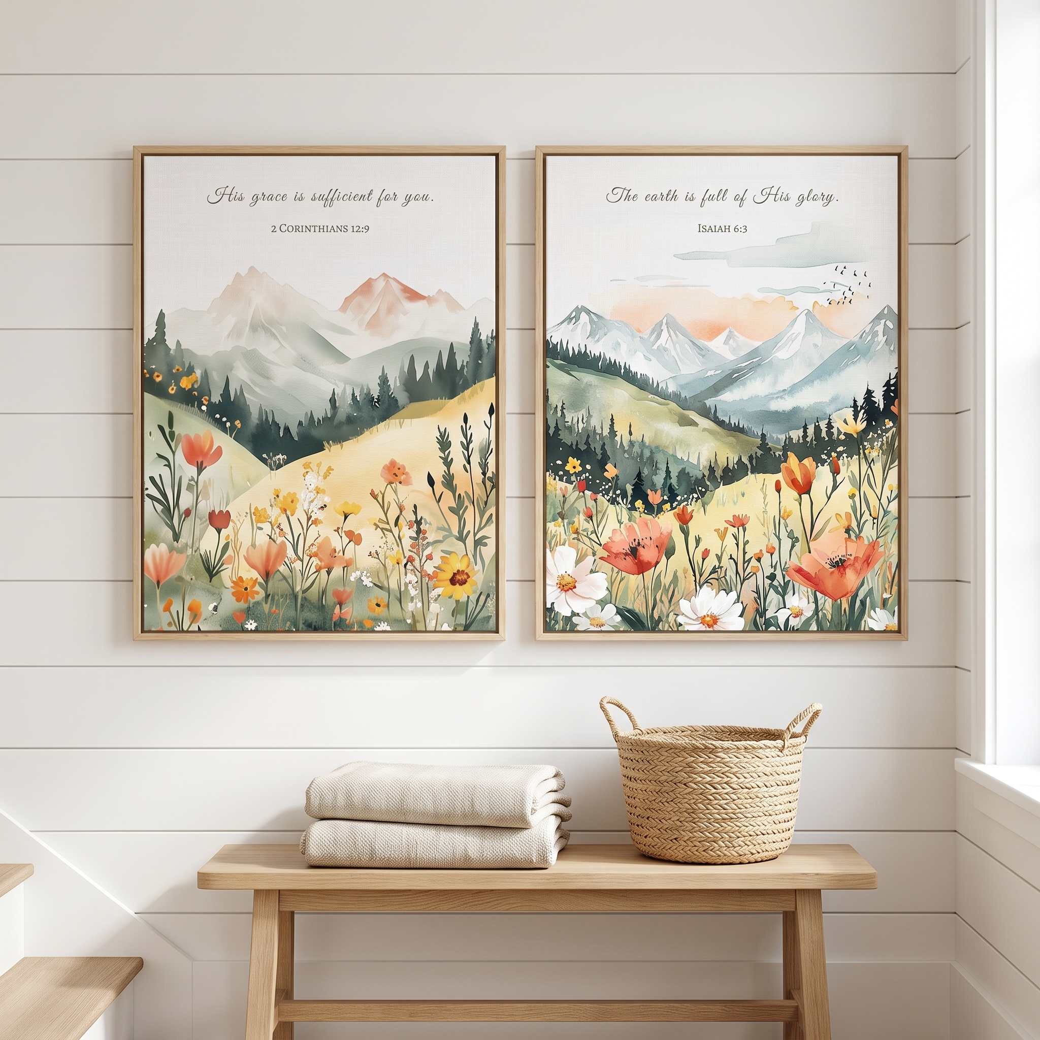 Two framed vintage Christian mountain landscape wall art prints featuring 2 Corinthians 12:9 and Isaiah 6:3 Scripture verses with wildflowers and evergreen forests, displayed side-by-side above a wooden bench in a bright, modern entryway.