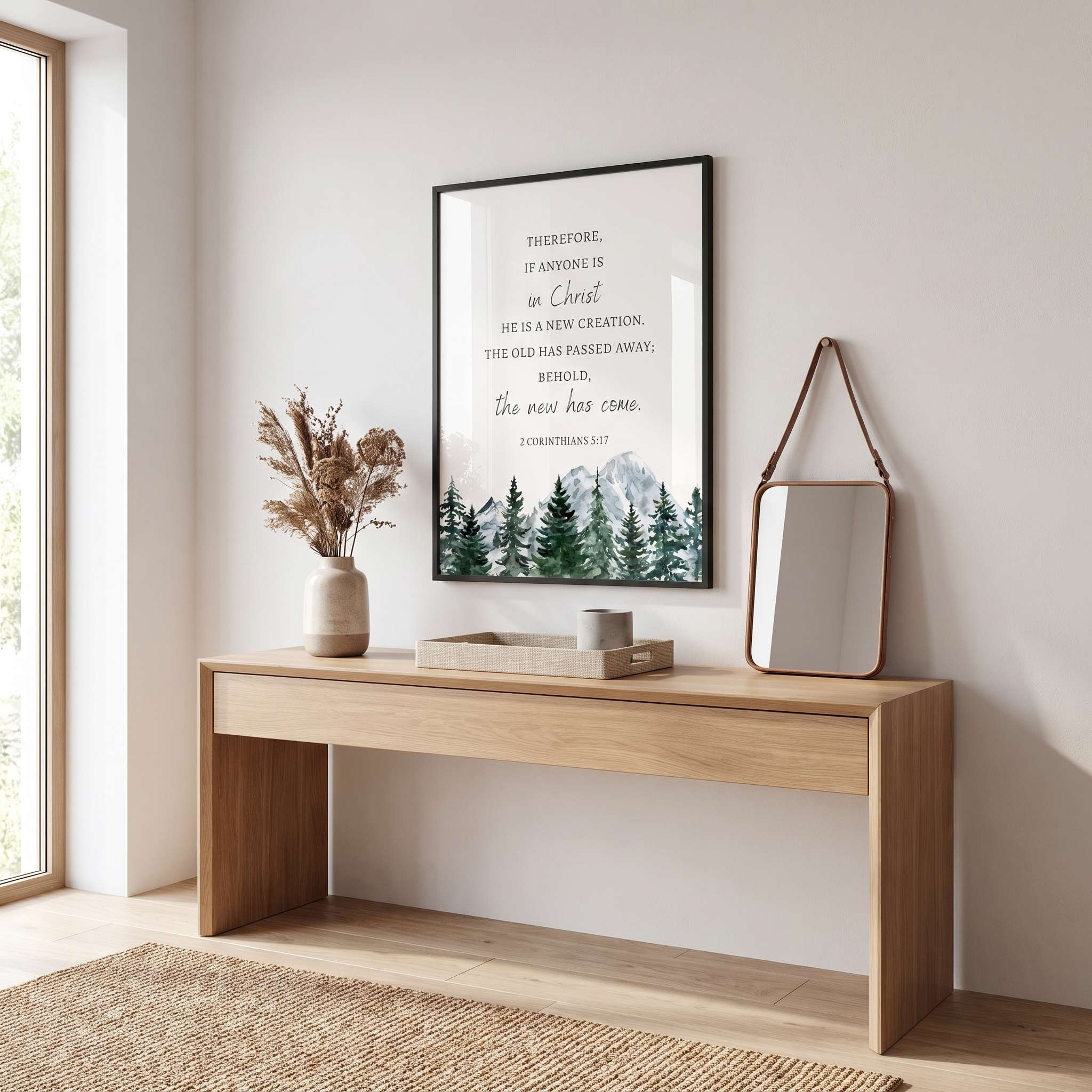 Framed 2 Corinthians 5:17 Christian wall art with a watercolor mountain forest and “If anyone is in Christ, he is a new creation” verse, displayed above an entryway console.