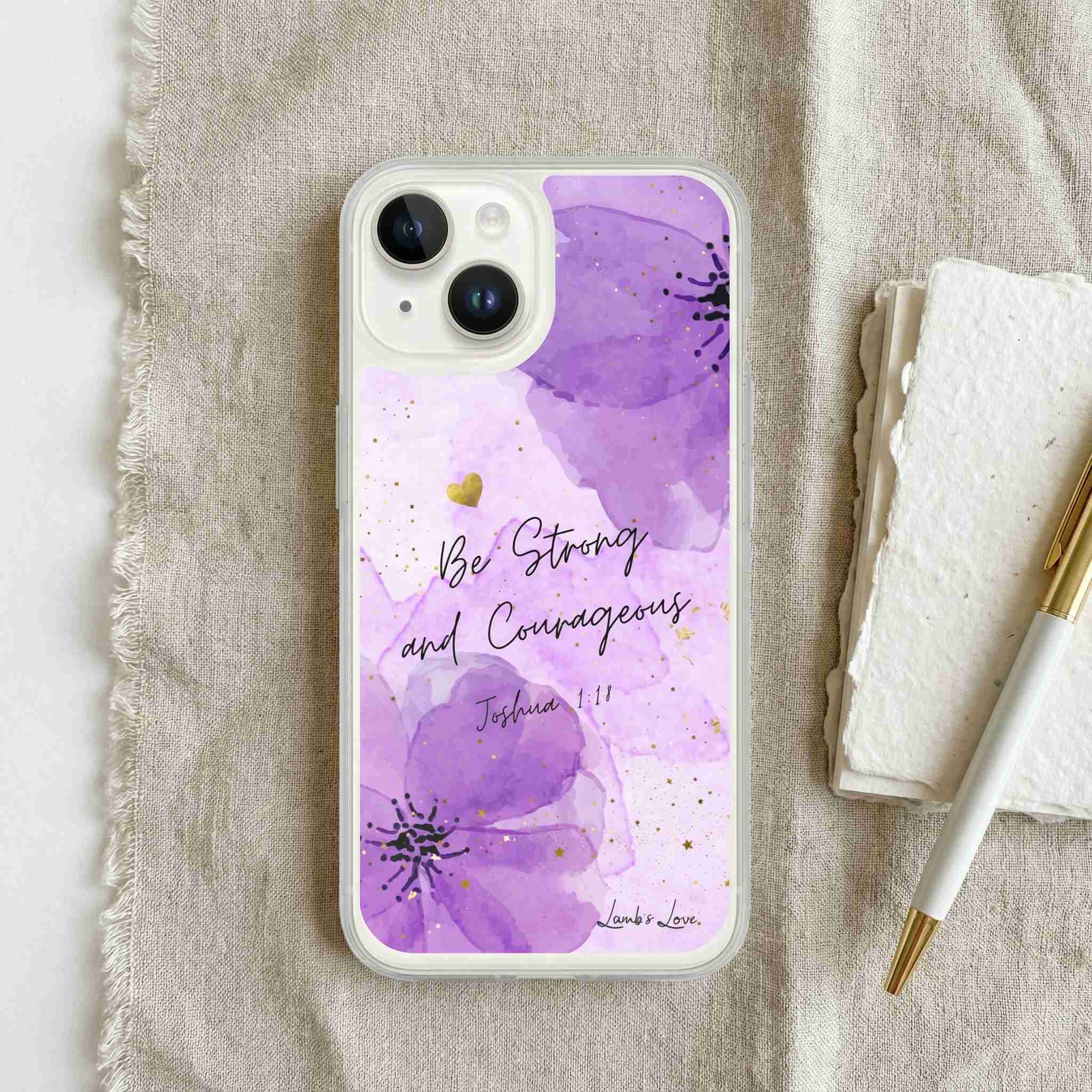 Phone case with purple floral design and 'Be Strong and Courageous' text on a textured surface.