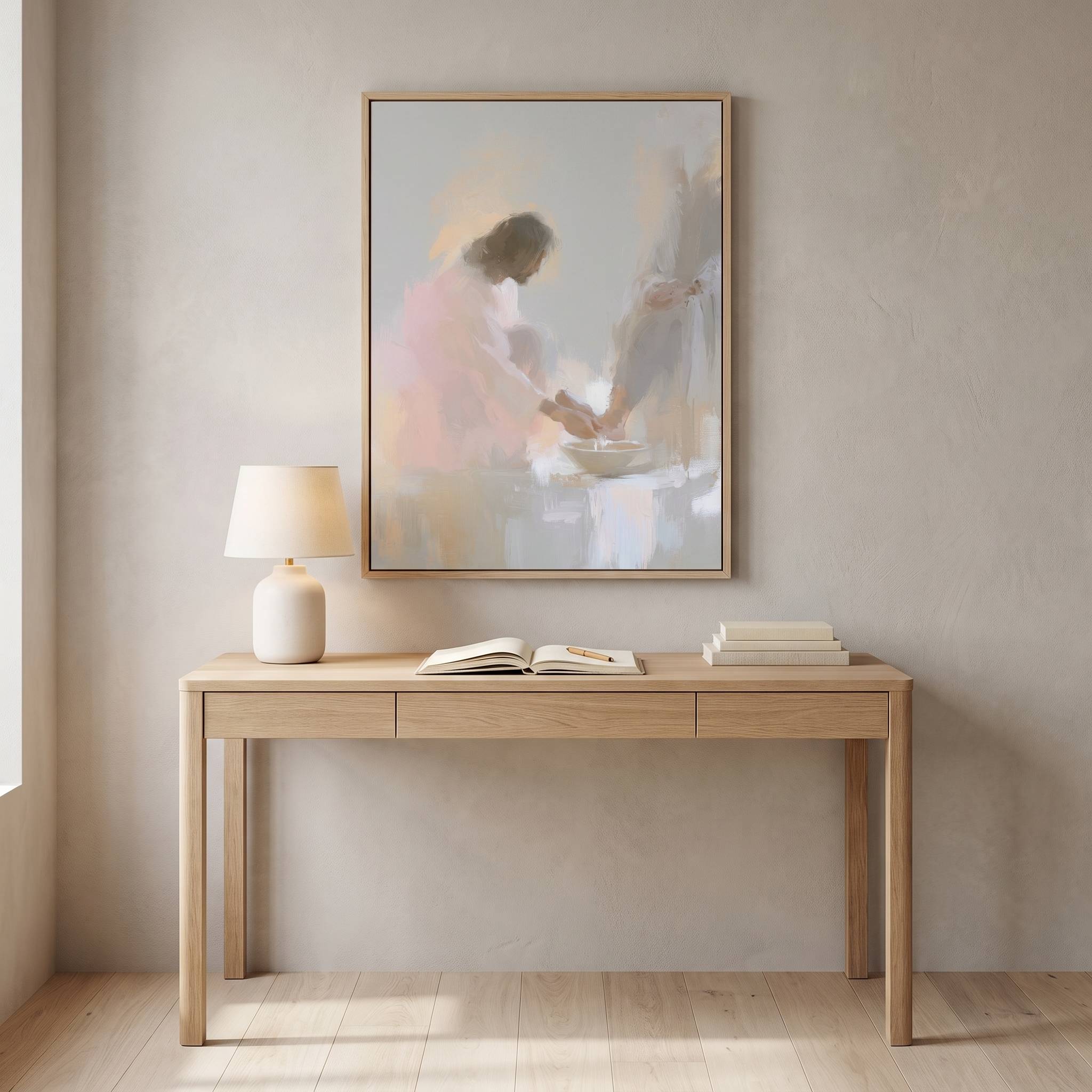 Framed Jesus washing feet watercolor art displayed above a light wood desk with books and a lamp in a neutral home office.