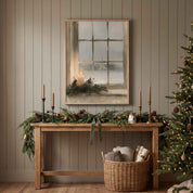 Vintage Christian Christmas wall art featuring a candlelit snowy window, displayed above a garland-covered console beside a lit Christmas tree.