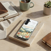 Be Still and Know Christian Samsung phone case with mountain landscape and wildflower design, displayed on a textured sandstone block next to an open Bible, a cup of coffee, and a small succulent.