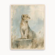 Be Strong and Courageous Christian kids wall art showing a watchful lion cub seated on a rock among grasses, with soft blue and beige tones and a light wood frame.