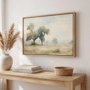 Framed vintage Jeremiah 17:7 Christian landscape canvas wall art hanging above a light wooden console table with stacked books and a pampas grass vase in a soft organic modern entryway.