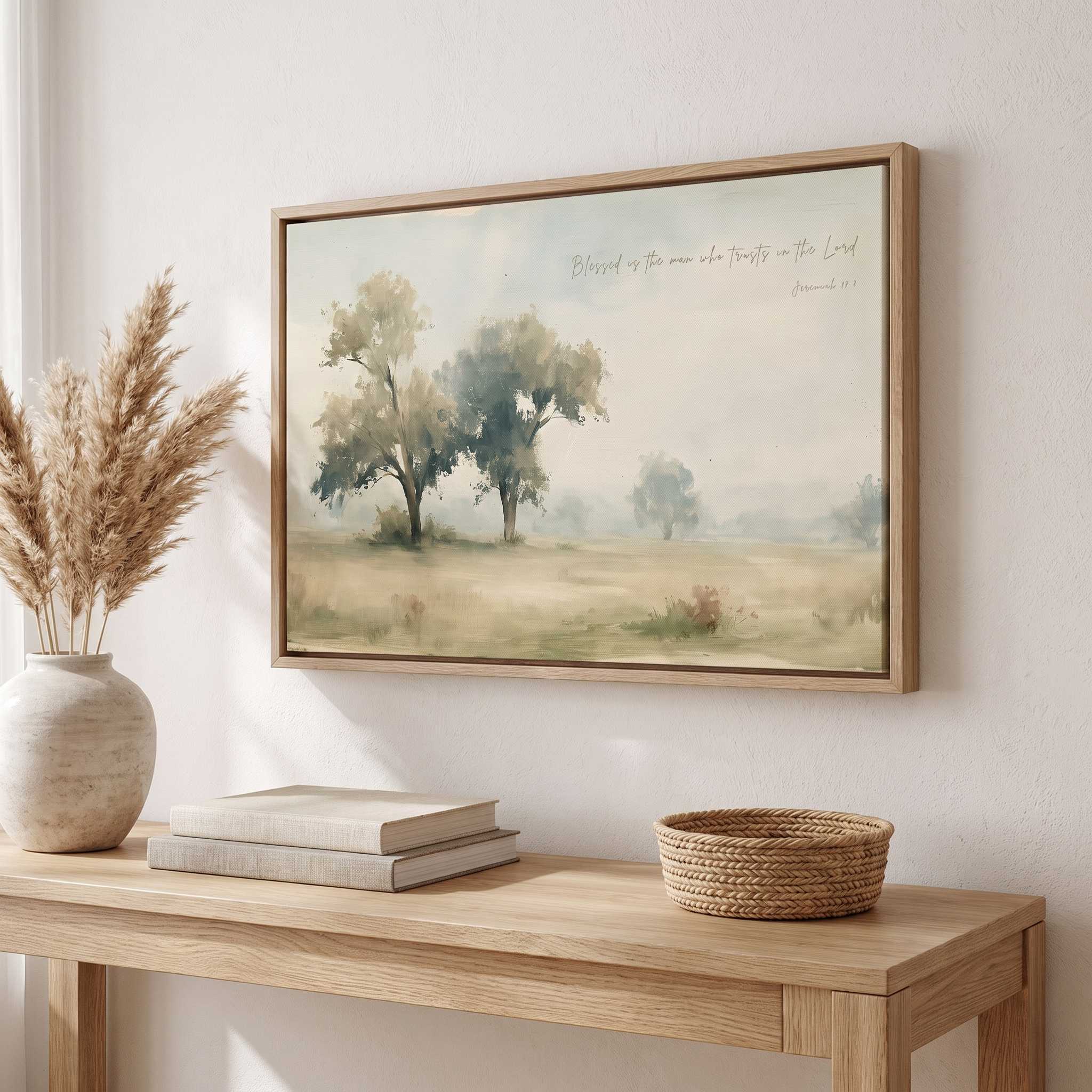 Framed vintage Jeremiah 17:7 Christian landscape canvas wall art hanging above a light wooden console table with stacked books and a pampas grass vase in a soft organic modern entryway.
