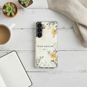 Chosen and Loved Christian Samsung phone case with yellow floral design on a white painted wood desk next to a coffee mug, succulent plant, and open notebook.
