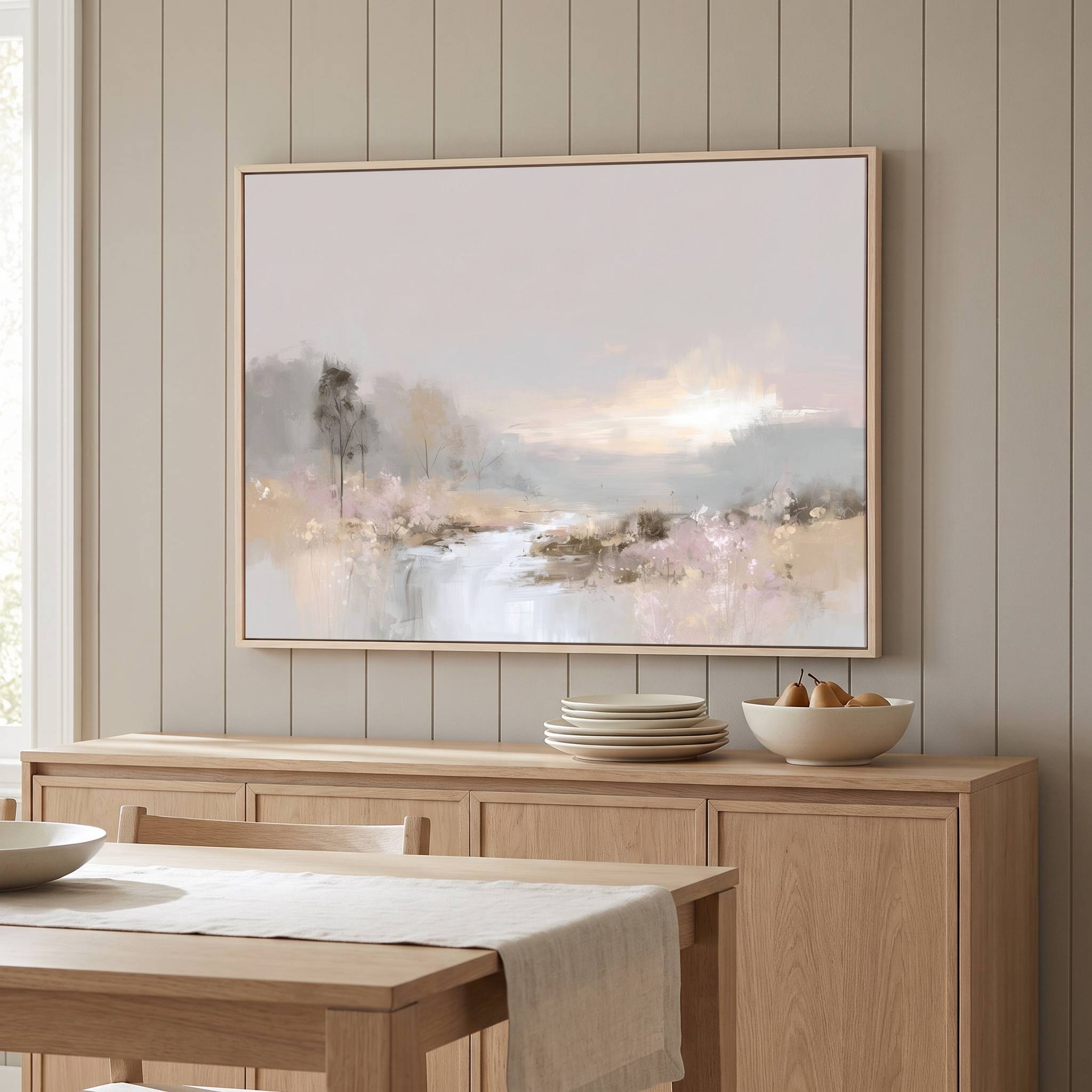 Framed watercolor Christian landscape wall art with a peaceful lake and soft sky, displayed above a light wood dining room sideboard with plates and a bowl.