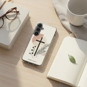 Minimalist Christian Samsung Galaxy case with a black cross and botanical design on a wooden desk next to an open journal, glasses, and a coffee mug