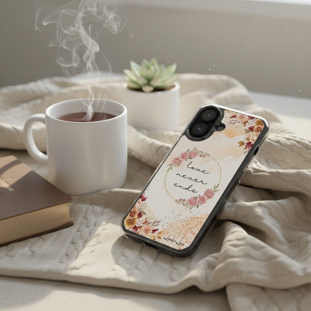Cozy morning devotional setting with a floral 'Love Never Ends' MagSafe iPhone case resting on a blanket next to a steaming cup of tea and a book.