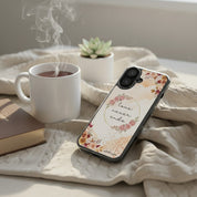 Cozy morning devotional setting with a floral 'Love Never Ends' MagSafe iPhone case resting on a blanket next to a steaming cup of tea and a book.