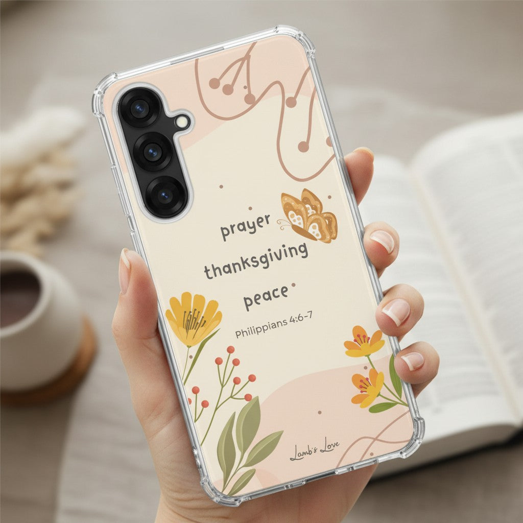 Close-up of a hand holding a Christian Samsung Galaxy phone case with "prayer thanksgiving peace" and Philippians 4:6-7 scripture, featuring a yellow floral and butterfly design.
