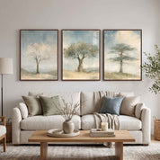 A three-piece framed Christian wall art triptych featuring the almond blossom, olive tree, and cedar of Lebanon prints displayed above a beige sofa in a neutral living room.