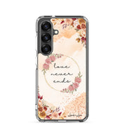 Love Never Ends Christian Samsung Galaxy S25 phone case with soft floral wreath design featuring 1 Corinthians 13:8 Bible verse on clear protective case