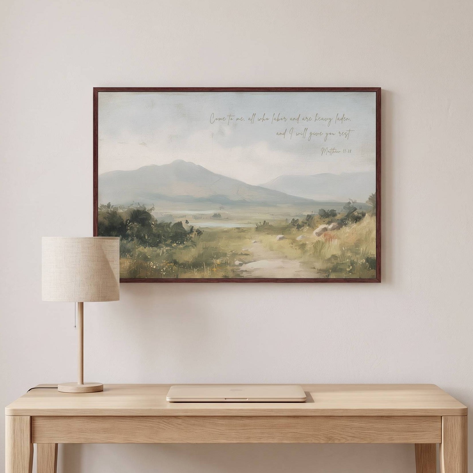 Framed vintage Christian landscape wall art titled Come to Me with Matthew 11:28 verse, displayed above a light wood desk with a table lamp in a modern home office.