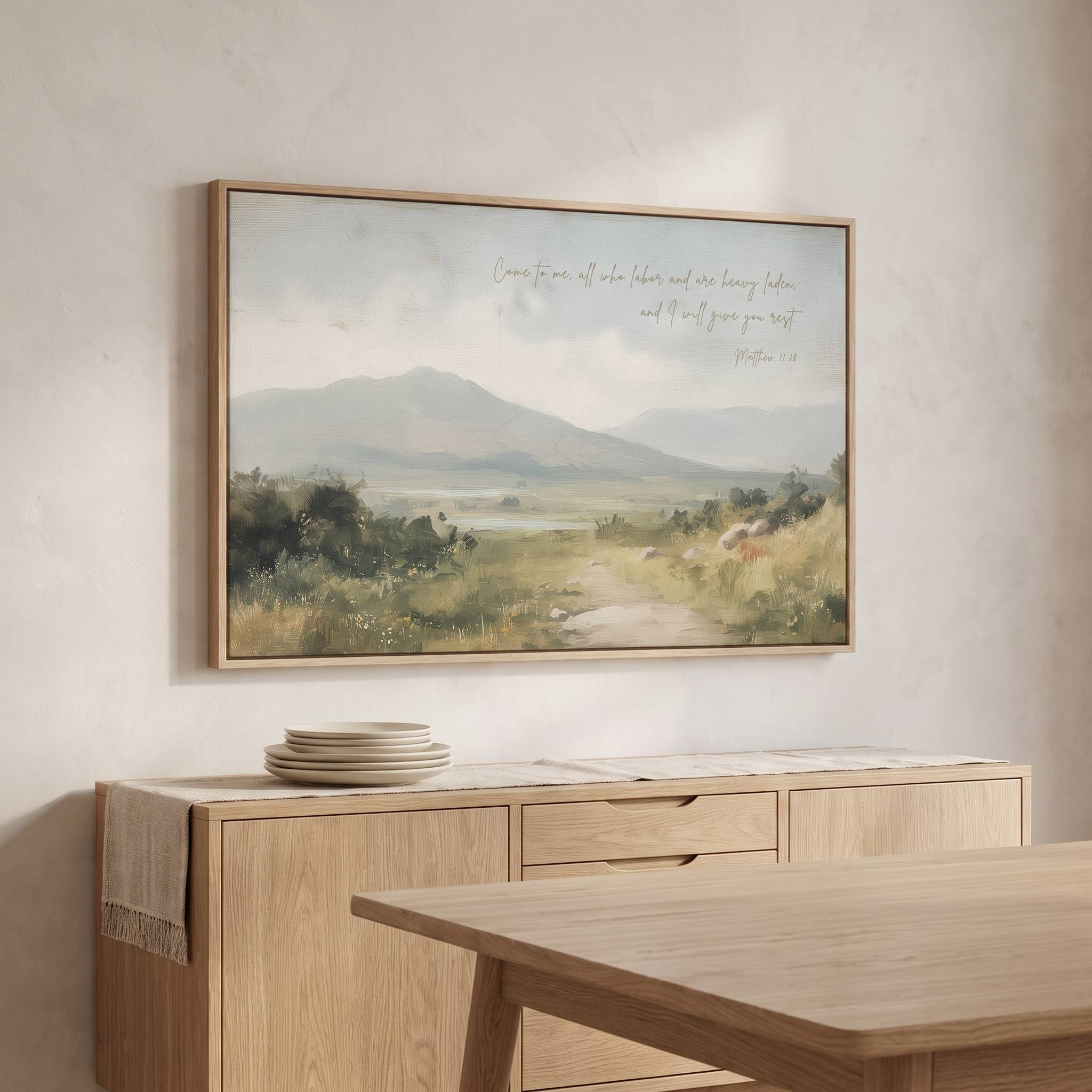Framed vintage Christian landscape wall art titled Come to Me with Matthew 11:28 verse, displayed above a light wood sideboard in an organic modern dining room.