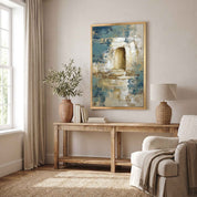 Contemporary Christian abstract empty tomb framed canvas wall art featuring a glowing open tomb motif in textured blue, beige, and gold brushstrokes displayed on a light wall above a wood console table in an organic modern living room.