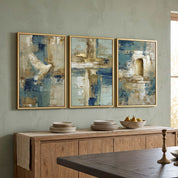Contemporary Christian abstract 3-piece framed canvas wall art set featuring white dove, cross, and empty tomb motifs in blue, beige, and gold displayed on a muted green wall above a wooden sideboard in an organic modern dining room.