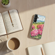 Faith Over Fear Christian Samsung phone case with pink floral landscape design, placed on a light wood desk next to an open Bible with a cross bookmark, a white coffee mug, and a small succulent.