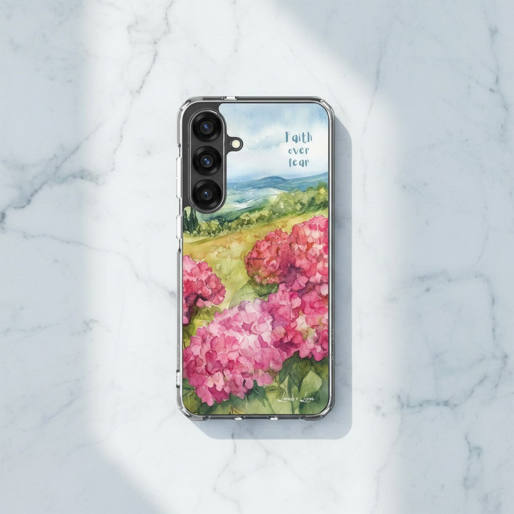 Faith Over Fear Christian Samsung phone case featuring a pink watercolor floral landscape with a blue sky and rolling hills, displayed on a white marble surface with soft shadows.