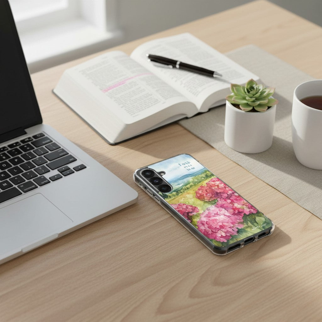 Faith Over Fear Christian Samsung phone case featuring a pink floral landscape design, placed on a wooden desk next to a laptop, an open Bible with a pen, a small succulent, and a white coffee mug.