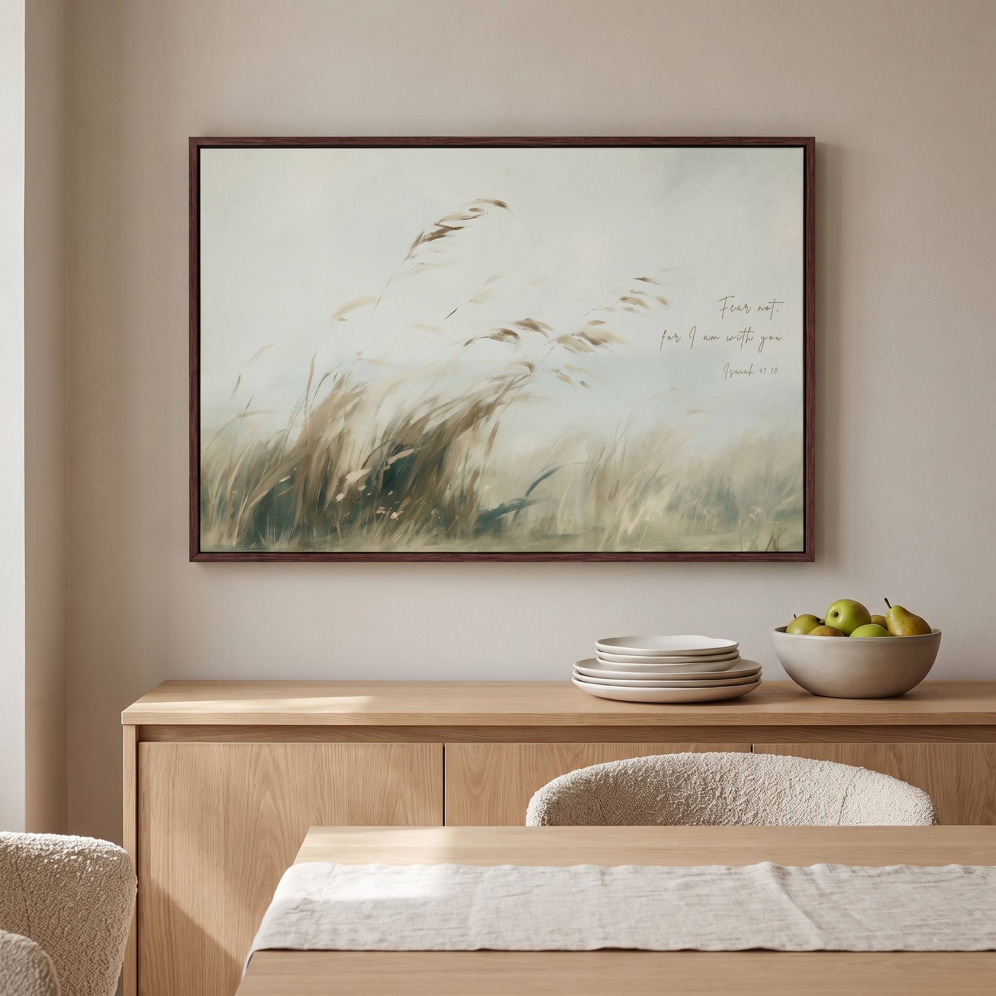 Framed vintage Isaiah 41:10 landscape canvas wall art hanging above a light wood sideboard with plates and a fruit bowl in a bright organic modern dining room.