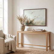 Framed vintage Isaiah 41:10 landscape canvas wall art hanging above a light wooden console table with a ceramic vase and armchair in a soft organic modern living room.
