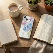 Phone case with floral design on a wooden table with a cup of coffee, notebook, and open book.