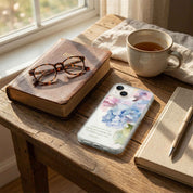 Phone with floral case on a wooden table with books, glasses, and a cup of tea.