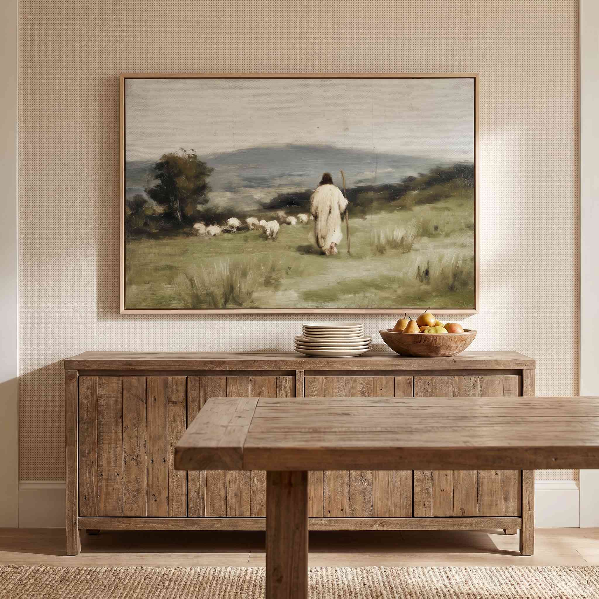 A framed landscape painting of a shepherd with sheep hangs on a textured beige wall above a rustic wooden sideboard, with a matching wooden dining table in the foreground.