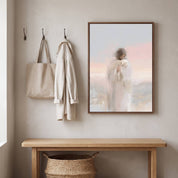 Framed watercolor Christian wall art of Jesus carrying a white sheep on a beige entryway wall above a wooden bench, styled with a woven tote and linen coat.