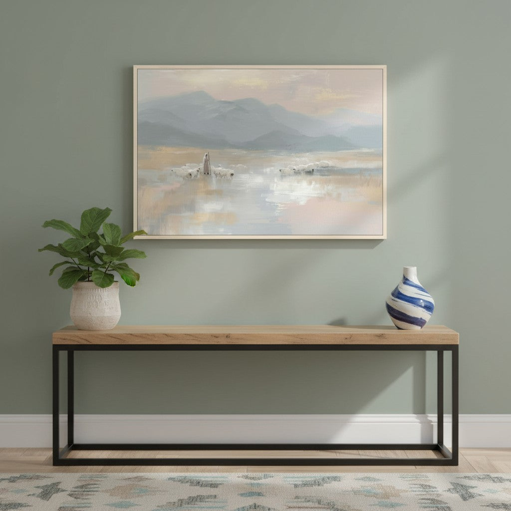 Framed Good Shepherd wall art of Jesus and His sheep on a misty mountain shore, displayed on a sage green wall above a console table.