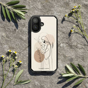 Good Shepherd Christian MagSafe iPhone case on natural stone surface surrounded by olive branches and wildflowers featuring minimalist artwork of Jesus holding a lamb with warm neutral faith-inspired aesthetic