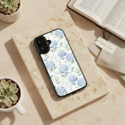 Grace in Bloom MagSafe® clear iPhone case featuring soft blue hydrangea floral artwork displayed beside an open Bible, linen fabric, and ceramic planters in a warm devotional lifestyle setting