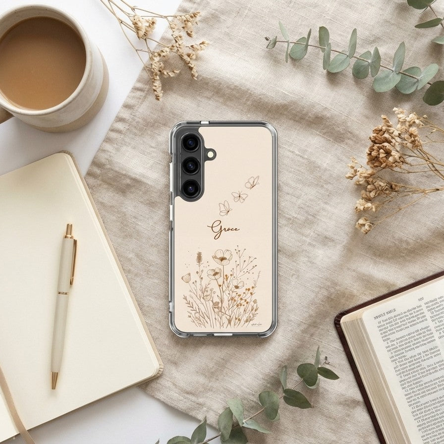 Grace Christian Samsung Galaxy phone case with wildflowers and butterfly design on desk with coffee, notebook, and open Bible faith lifestyle scene