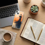 Laptop, phone with a scenic case, open book, pen, and coffee on a wooden desk.