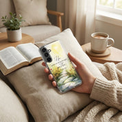 Person holding a Samsung galaxy phone with a scenic case on a cozy living room couch.