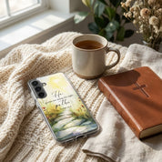 Samsung galaxy with a beautiful christian case, mug of tea, and leather-bound book on a textured surface near a window.