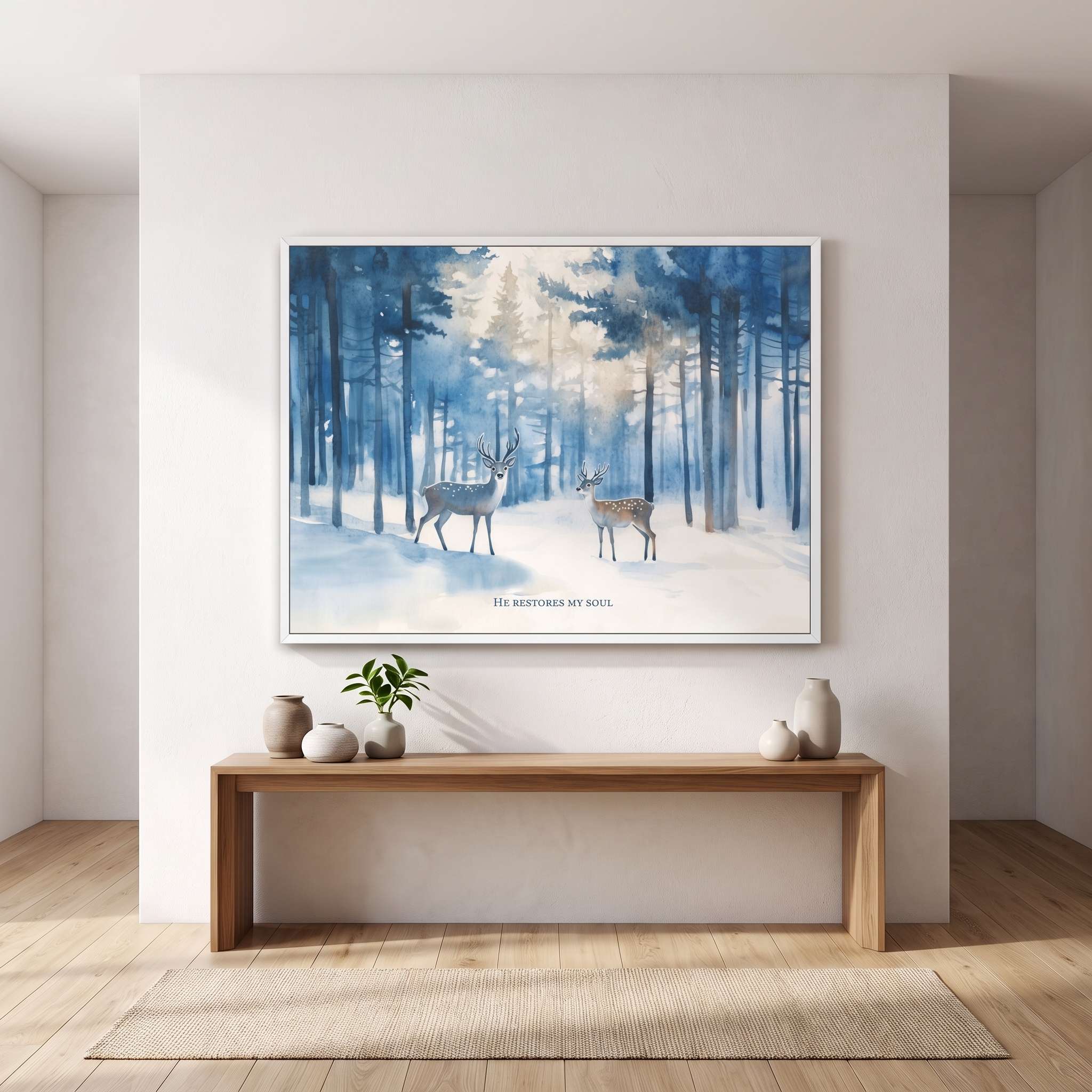 A framed art print depicting two deer in a snowy forest hangs on a white wall above a wooden console table in a minimalist room setting.