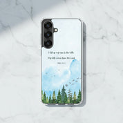 I Lift Up My Eyes Christian Samsung Galaxy phone case with a blue watercolor mountain landscape and Psalm 121:1-2 Bible verse, displayed on a white marble surface.
