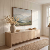 Framed vintage Christian landscape wall art titled I Lift Up My Eyes to the Hills, displaying a peaceful mountain view above a light wood credenza in a bright hallway.