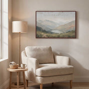 Framed vintage Christian landscape wall art titled I Lift Up My Eyes to the Hills, displaying a peaceful mountain view above a beige armchair in a cozy reading nook.