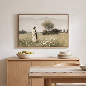 A framed landscape art print depicting Jesus walking in a field, displayed on a light wood sideboard in a minimalist dining room setting.