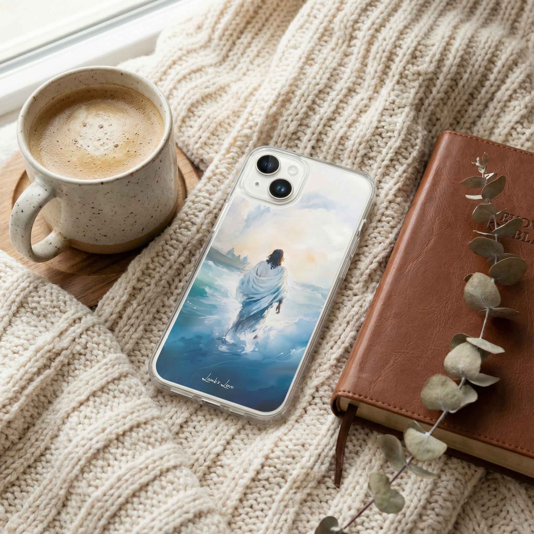 Phone case with a design of Jesus walking on water, next to a cup of coffee and a notebook.