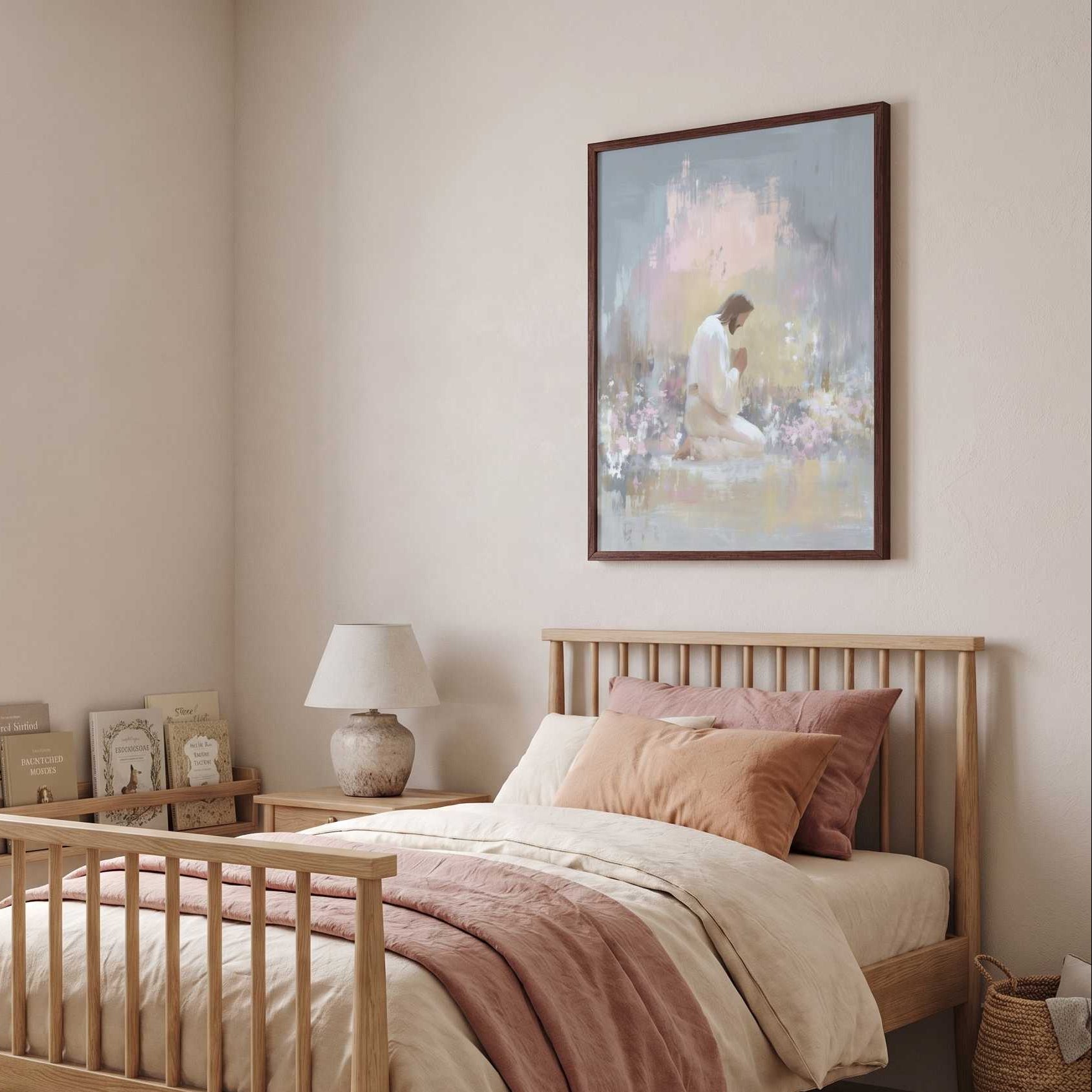 Framed Jesus praying in Gethsemane wall art above a nursery bed with blush bedding, showing Christ kneeling in a soft watercolor garden.