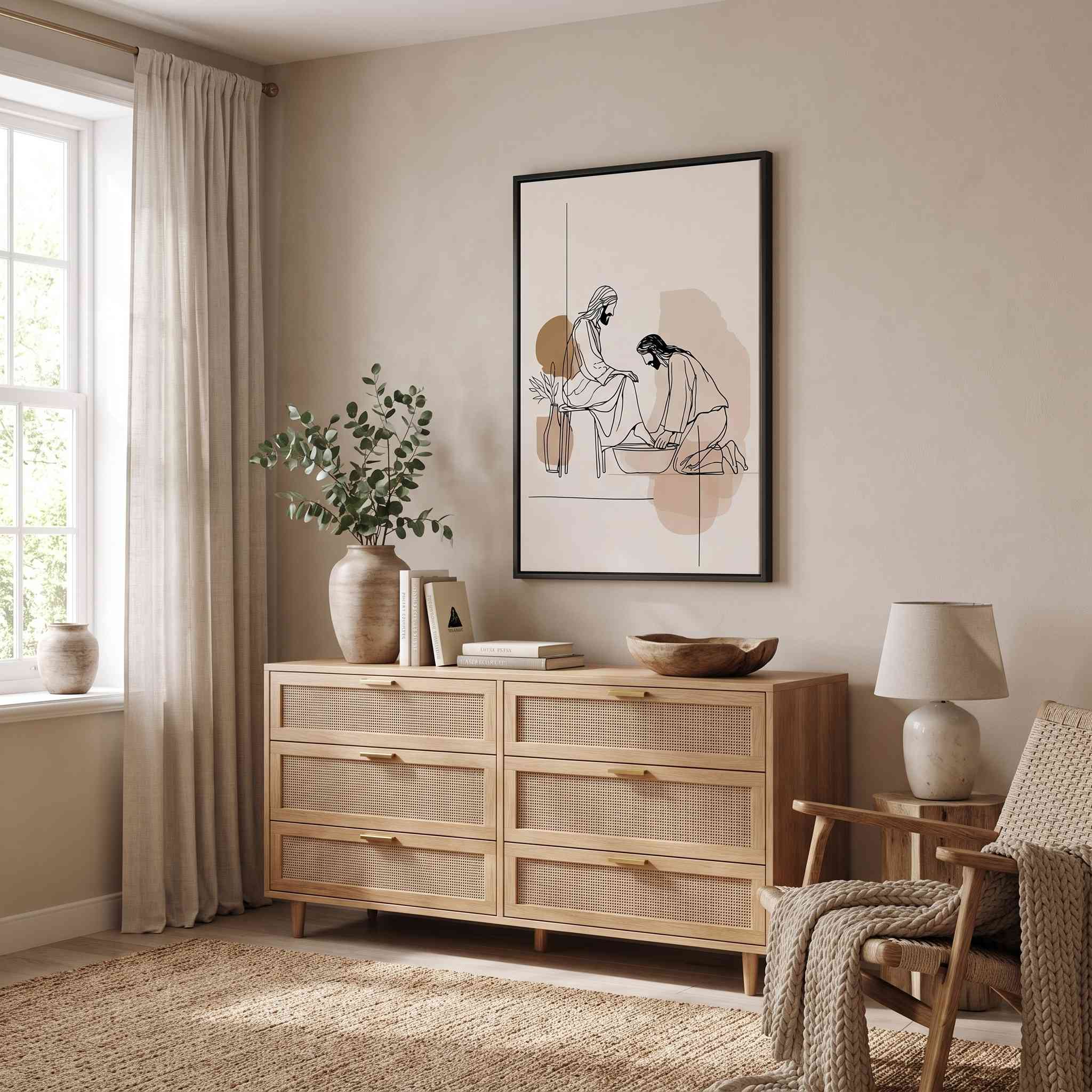 Minimalist line art print of Jesus washing feet in a black frame hanging on a beige wall above a cane wood dresser in a modern bedroom.