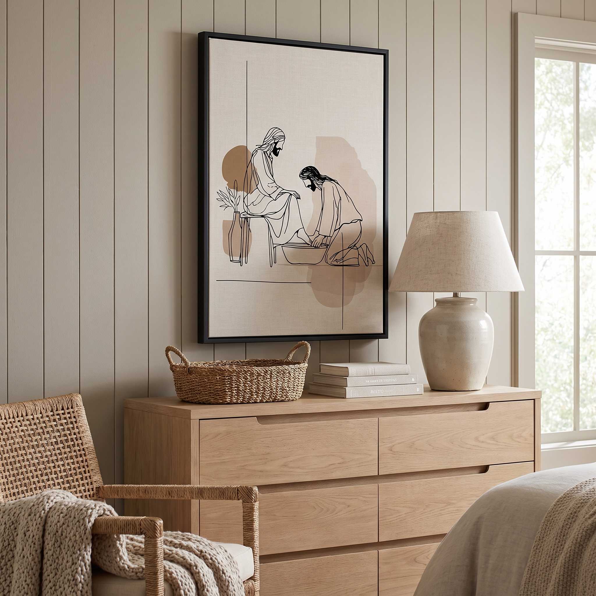 Minimalist line art print of Jesus washing feet in a black frame hanging on a light wood-paneled wall above a beige wooden dresser in a bedroom setting.
