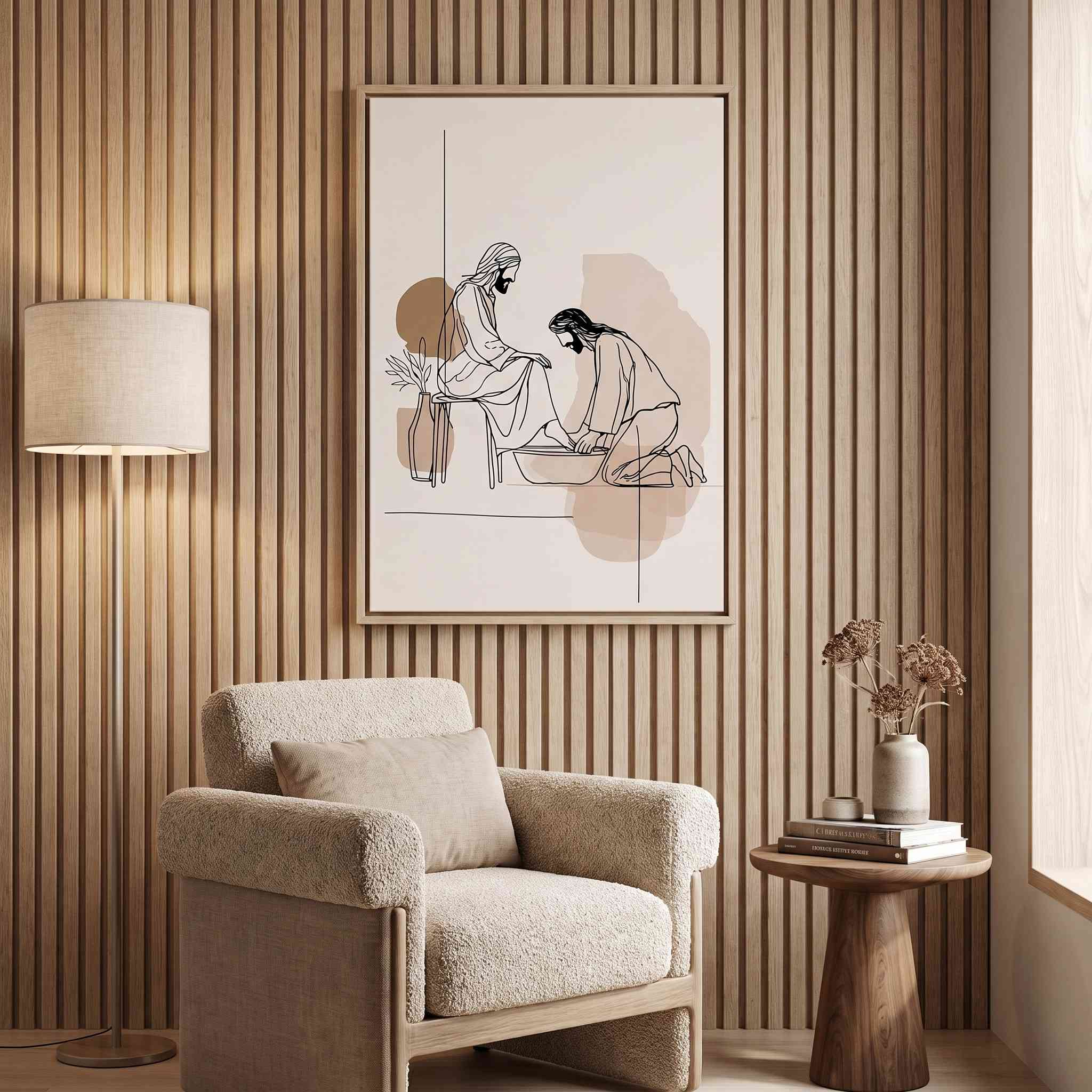Minimalist line art print of Jesus washing feet in a light wood frame hanging on a slatted wood wall above a cozy beige armchair.