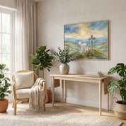 John 1:29 Lamb of God watercolor wall art showing a lamb beside a cross at sunrise, displayed above a console in a bright sunroom with plants.
